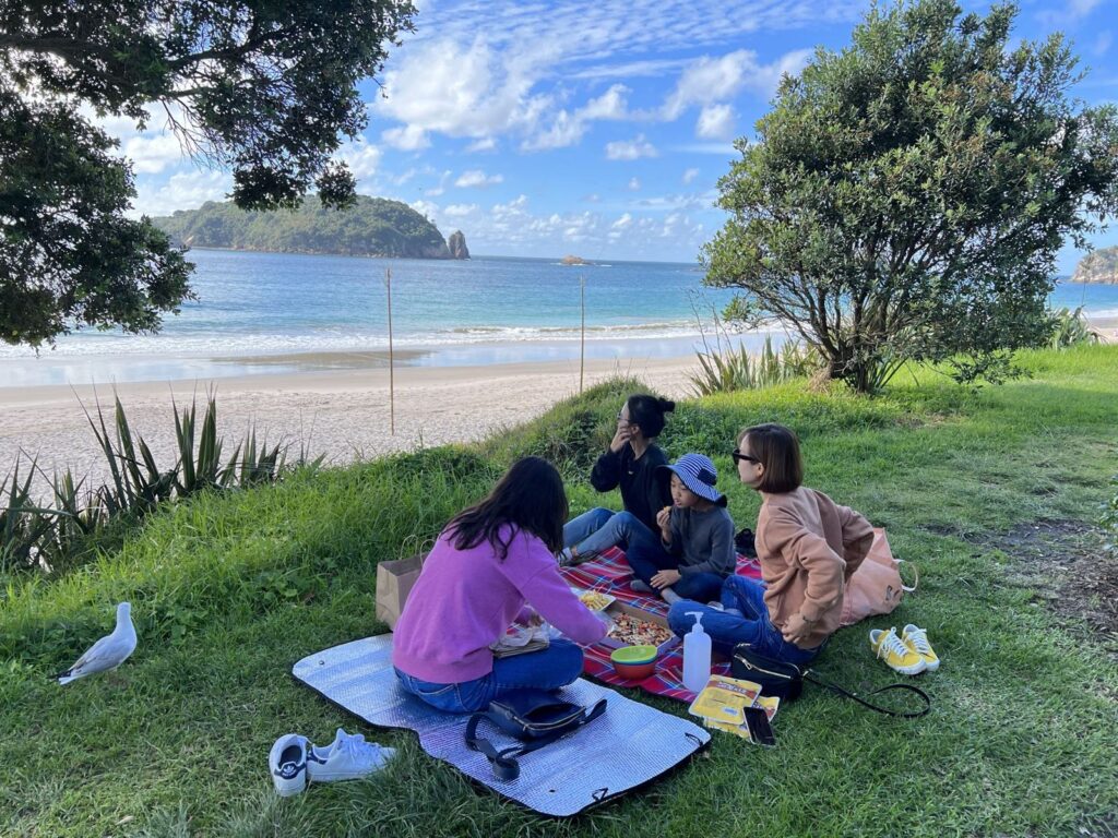 Travellers picnicking on a mat on the grass by the sea