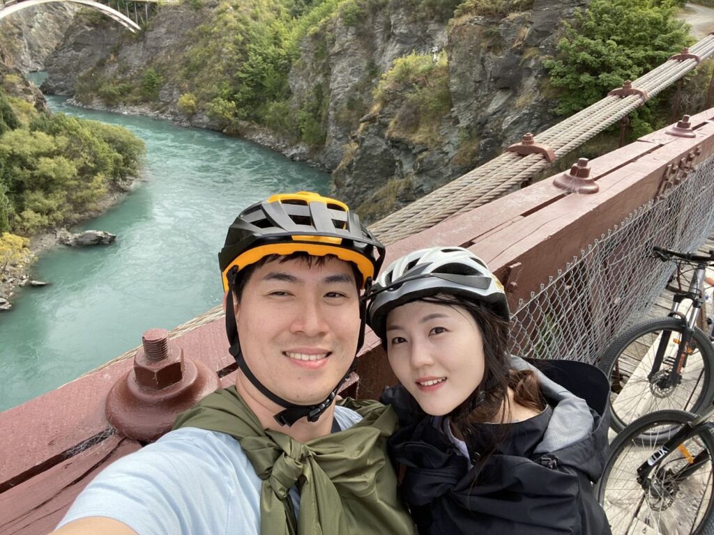 카와라우 다리 위에서 자전거 헬멧을 쓰고 웃는 두 여행자
